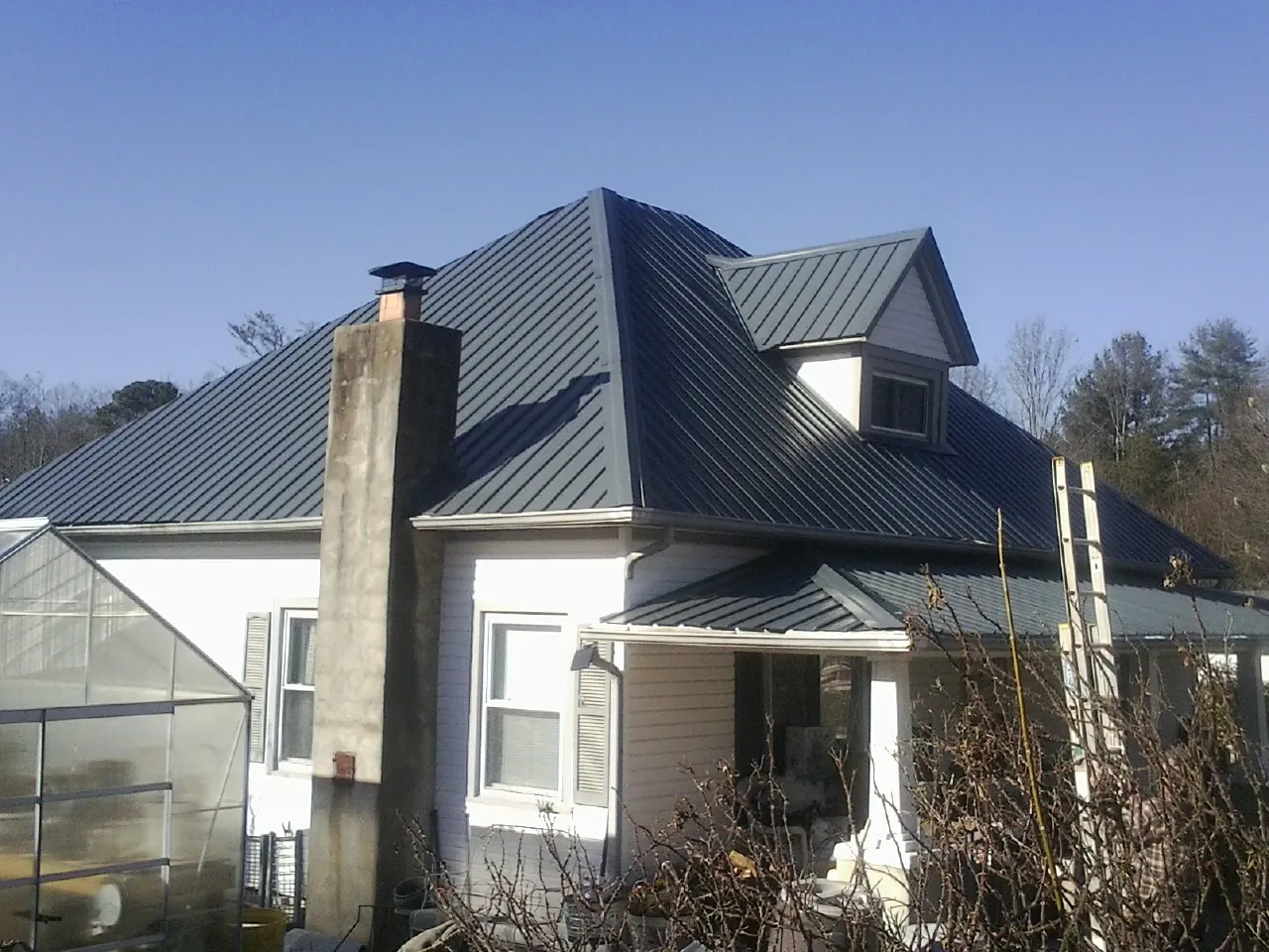 Dark blue standing seam metal roof on a white farmhouse with dormer — Slate & Tile Roof Repair by Roofing Brothers in Rush Springs