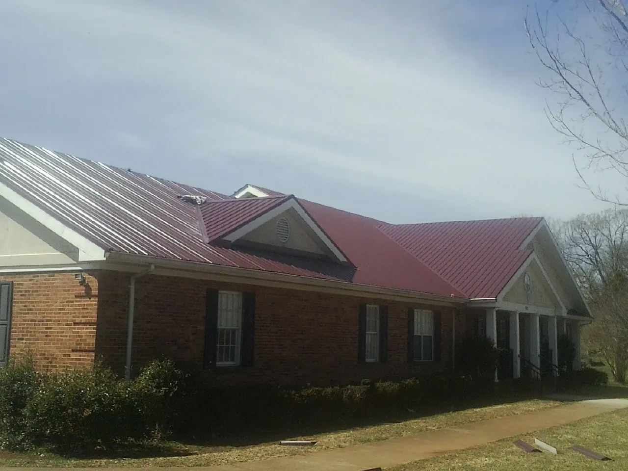 Red metal roof with gabled entries on a long brick building, from a Hail Damage Roof Repair job in Rush Springs