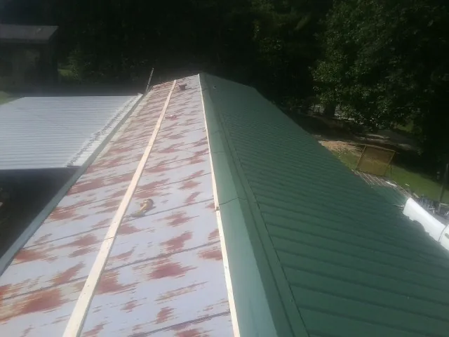 Old rusted panels beside newly installed green metal roofing — Wind Damage Roof Repair by Roofing Brothers in Rush Springs