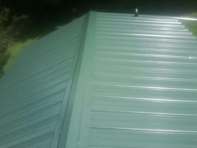 New green metal panels meeting at the ridge of a roof — Flat Roof Repair work by our crew in Rush Springs