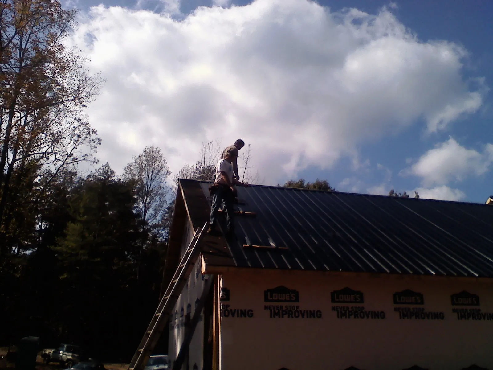 Roofer fastening dark metal panels high against a cloudy sky, from a Roof Inspection job in Rush Springs