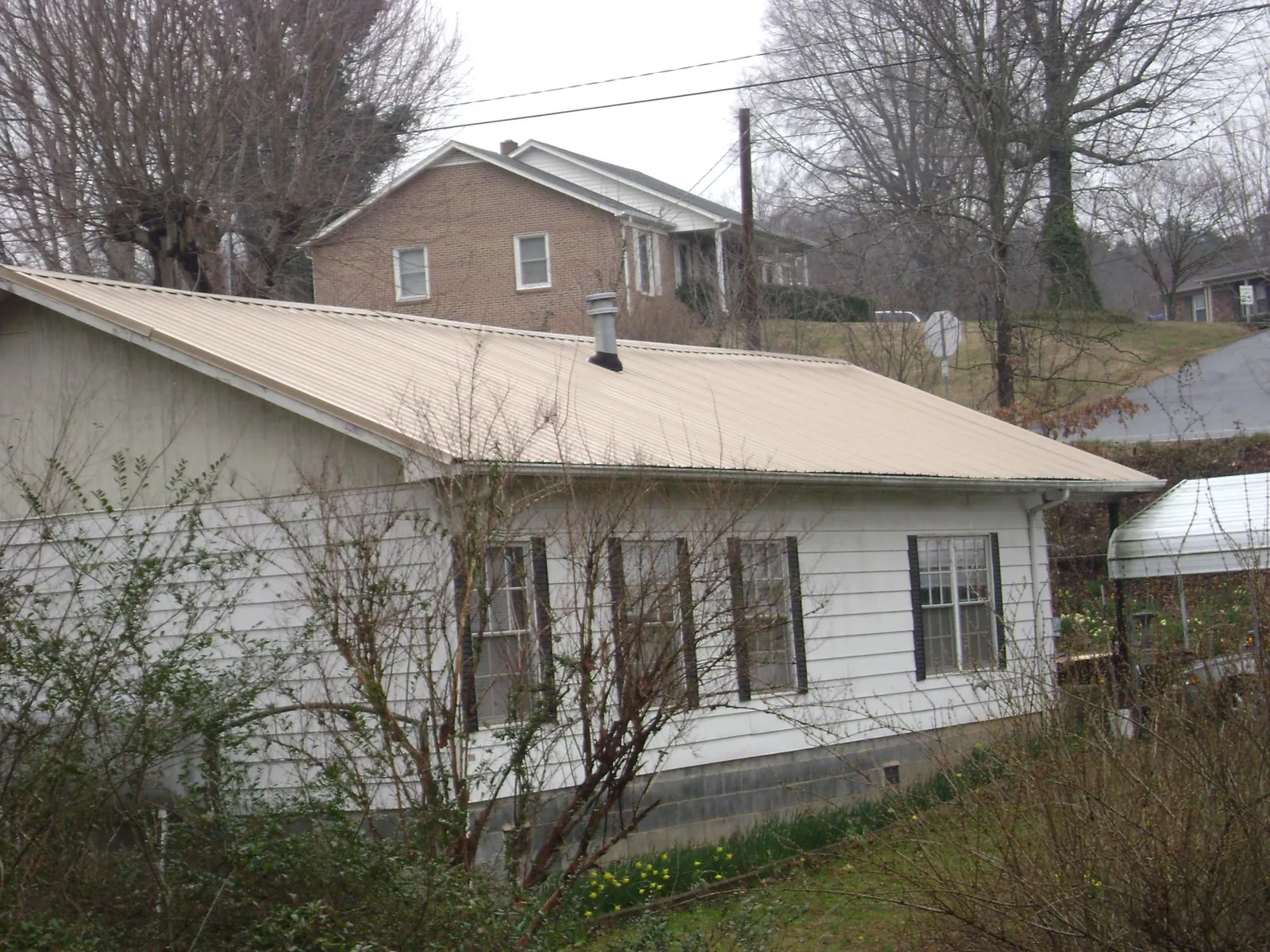 Tan metal roof on a white sided house set into a hillside — Commercial Roofing by Roofing Brothers in Rush Springs