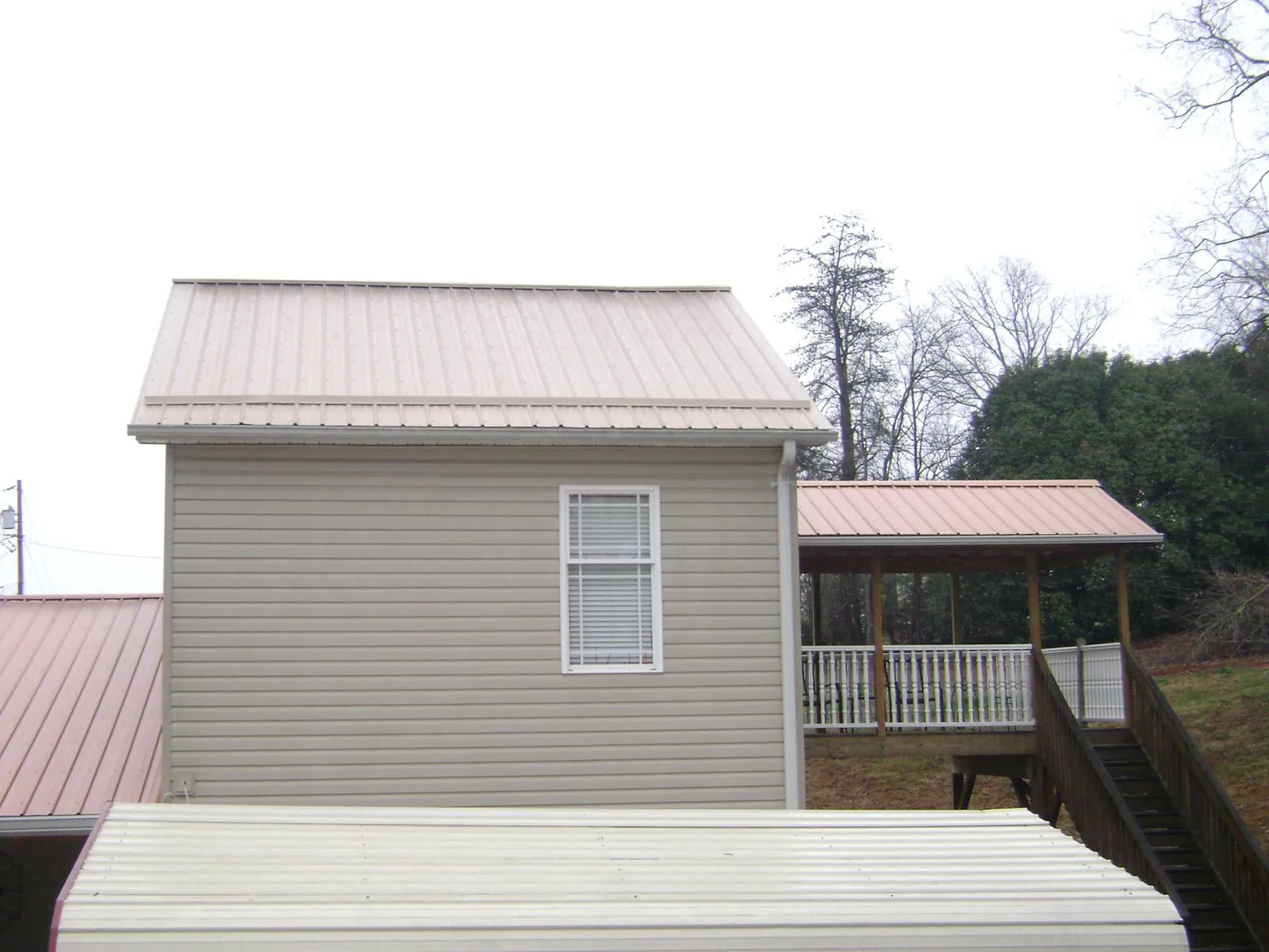 Tan metal roofs on a two story addition and attached porch, from a Roof Replacement job in Rush Springs